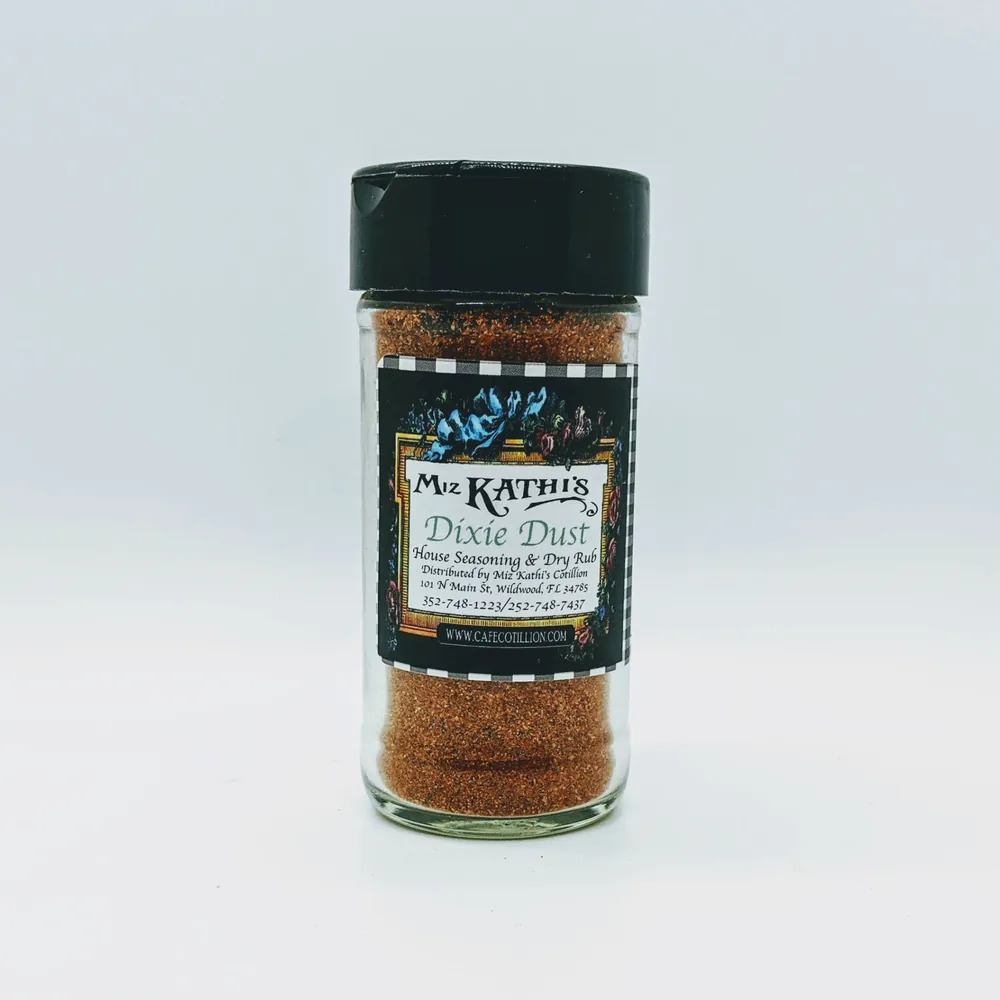A glass shaker jar of Miz Kathi’s Dixie Dust house seasoning and dry rub, with a black lid and the house floral label